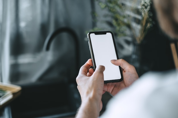 Homem usando smartphone com uma tela branca em branco na cozinha.