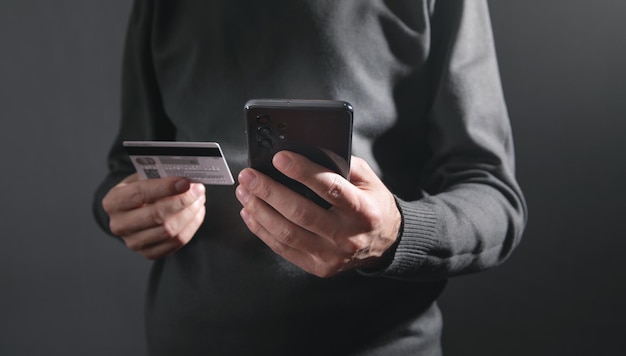 Homem usando smartphone e segurando o cartão de crédito.