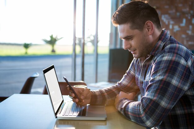 Homem usando telefone celular com o laptop na mesa