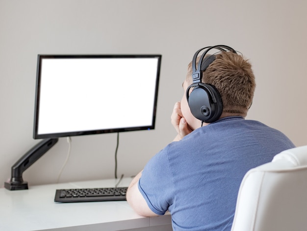 Homem usando, trabalhando em um computador com tela em branco na sala de estar de casa, conceito de dependência de internet