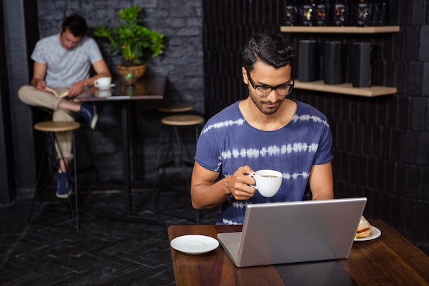 Homem usando um laptop e bebendo café