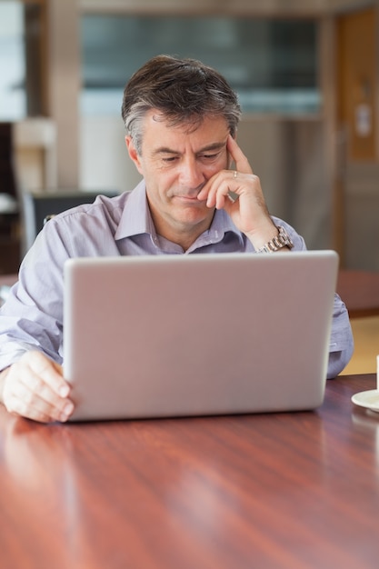 Homem usando um laptop em uma cafeteria e pensando