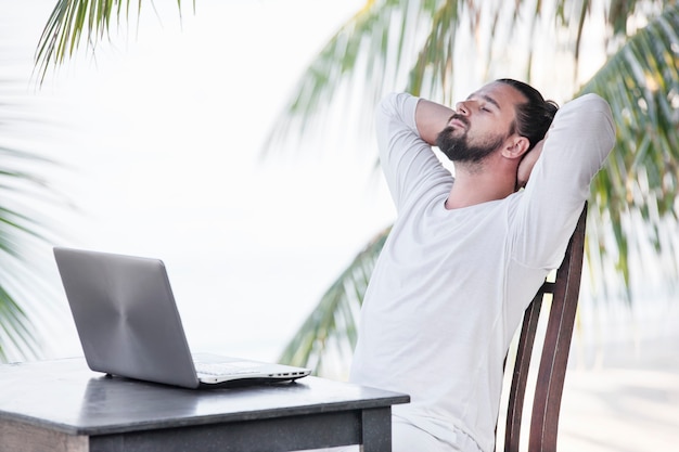 Homem usando um laptop enquanto está sentado no café da praia perto de palms