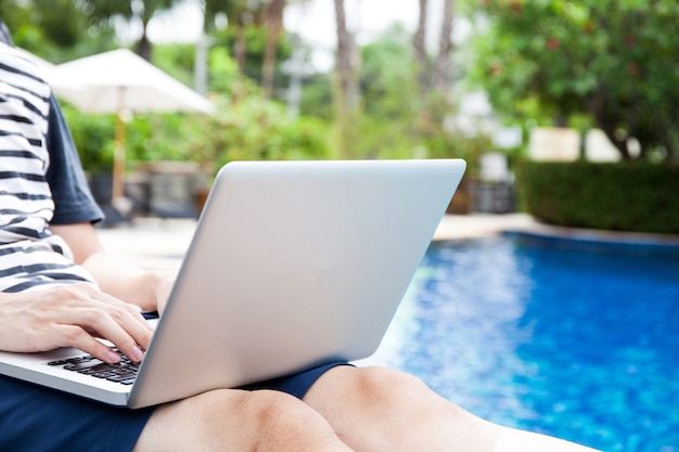 Homem usando um laptop na piscina de férias