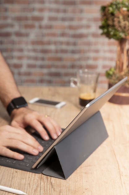 Homem usando um tablet para trabalhar, em uma mesa de madeira com uma xícara de café, em frente a uma parede de tijolos