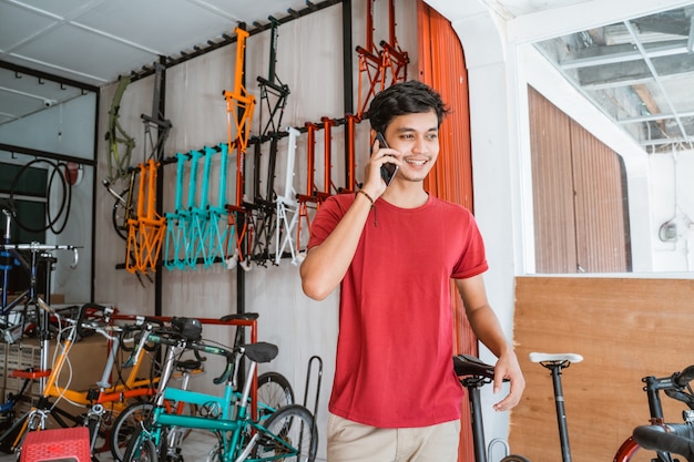 Homem usando um telefone celular para fazer uma chamada enquanto segura uma bicicleta nova na loja de bicicletas