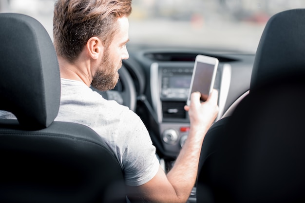 Homem usando um telefone inteligente, sentado no banco da frente do carro. Visão traseira focada no rosto