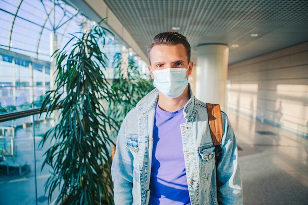 Homem usando uma máscara para prevenir o vírus no saguão do aeroporto internacional, esperando o avião do vôo.