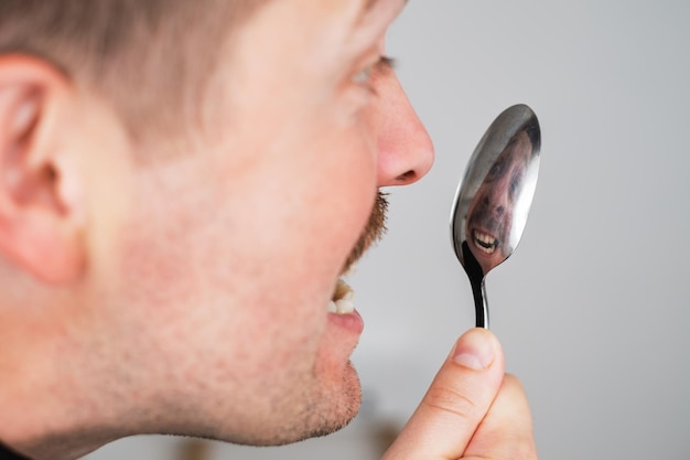 Homem verificando os dentes após a refeição olhando para seu reflexo na colher