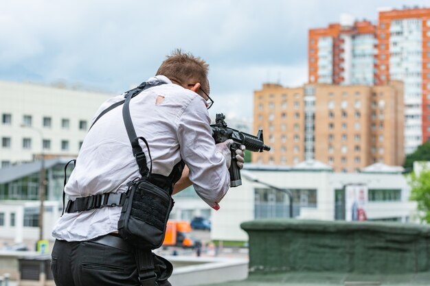 Homem vestido com um colete à prova de balas, uma camisa no sangue, persegue uma vítima com uma arma. estilo de filme de ação