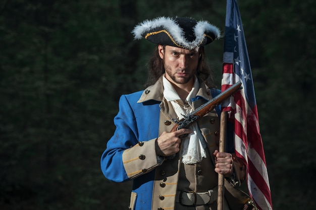 homem vestido como soldado da guerra da independência dos Estados Unidos visa pistola com bandeira
