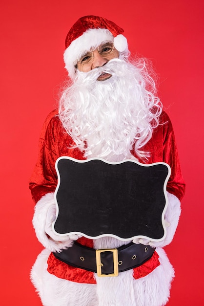 Homem vestido de Papai Noel segurando uma placa preta sobre fundo vermelho Presentes de celebração de Natal consumismo e conceito de felicidade