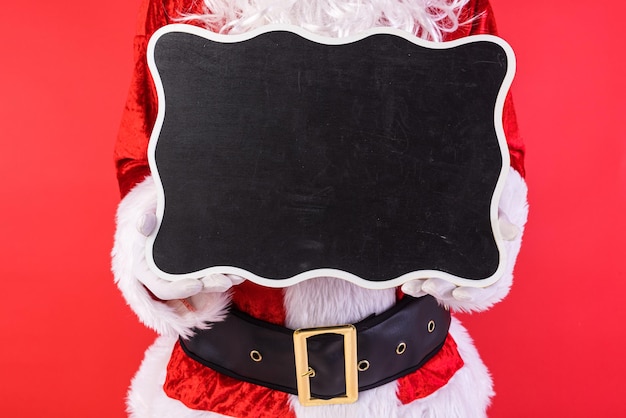 Homem vestido de Papai Noel segurando uma placa preta sobre fundo vermelho Presentes de celebração de Natal consumismo e conceito de felicidade