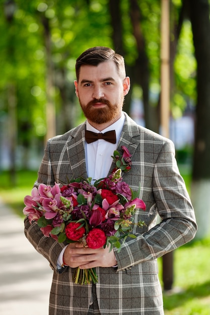 Homem vestido de terno elegante segurando buquê de flores