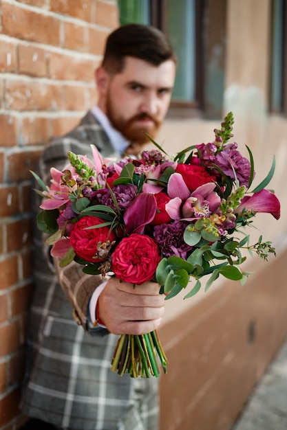 Homem vestido de terno elegante segurando buquê de flores