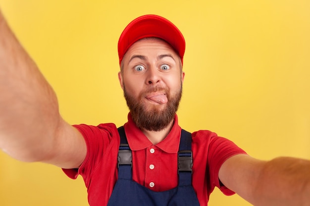 Homem vestindo boné e uniforme azul tirando selfie olhando para a câmera e mostrando a língua POV
