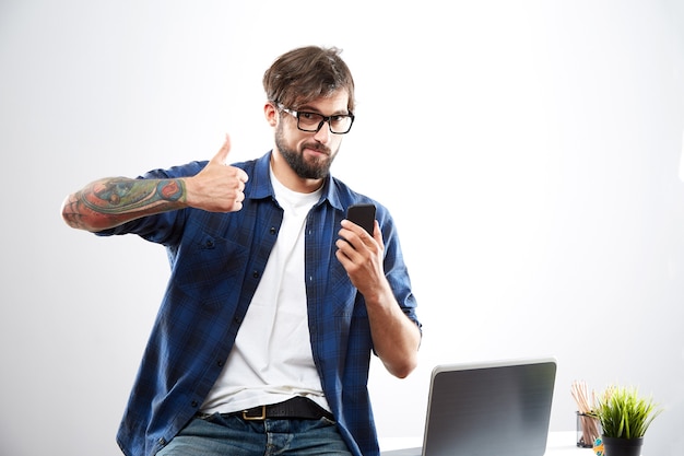 Homem vestindo camisa azul e óculos sentado com o laptop, conceito freelance, retrato, trabalho online, feliz, mostrando o polegar grande, super emoção.