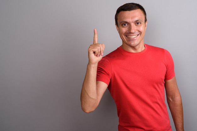 Homem vestindo camisa vermelha contra parede cinza