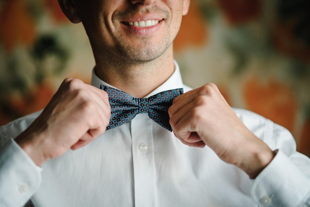 Homem vestindo gravata borboleta em uma camisa no conceito de roupa de quarto Homem fashion corrigindo gravata borboleta em uma camisa Noivo de preparação matinal em casa Close-up