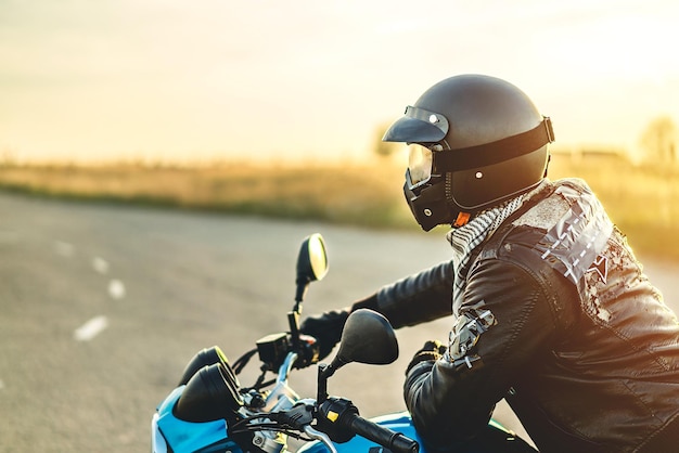 Homem vestindo jaqueta preta sentado em motocicleta durante o pôr do sol