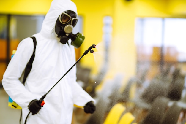 Homem vestindo roupa de proteção, desinfetando a sala de reuniões com produtos químicos em spray para prevenir o coronavírus.