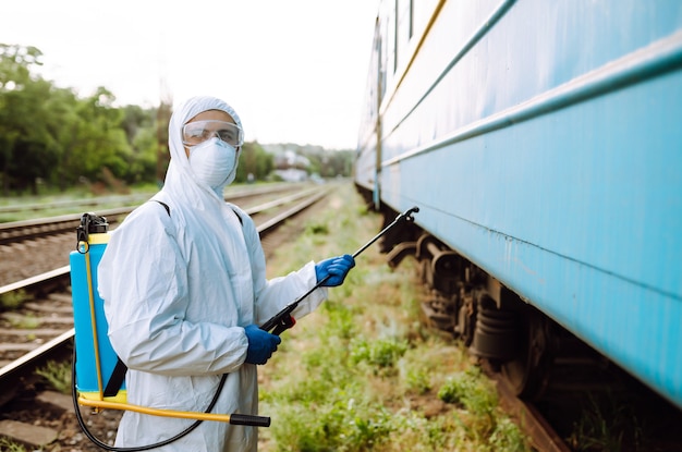 Homem vestindo roupa de proteção, desinfetando um trem público.