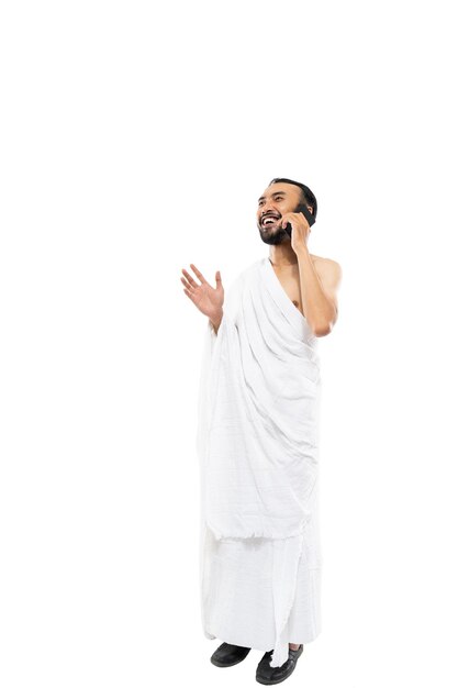 Foto homem vestindo roupas ihram usando smartphone para fazer uma chamada em fundo branco