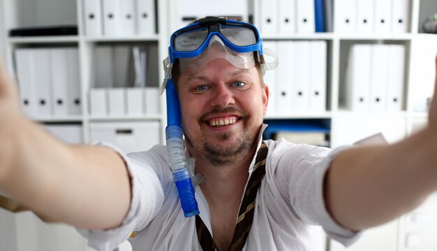 Homem vestindo terno e gravata em óculos e snorkel faz selfie com celular no escritório pronto para tirar o retrato Contar dias para sair do dia anual de folga workaholic liberdade diversão turismo resort ideia conceito