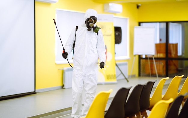 Homem vestindo traje de proteção desinfetando a sala de montagem com spray químico para prevenir o coronavírus