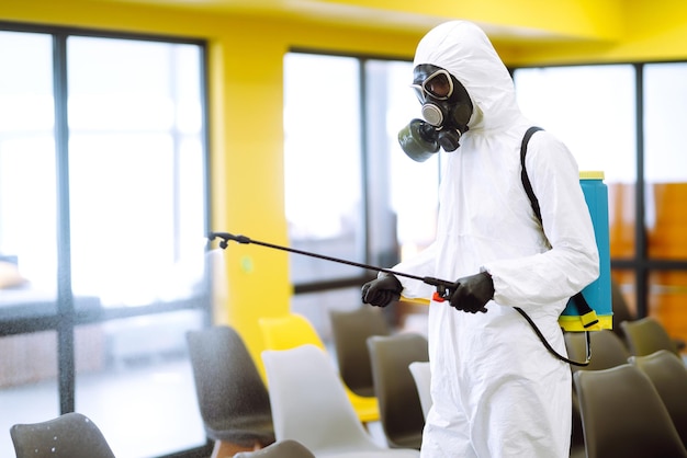 Homem vestindo traje de proteção desinfetando a sala de montagem com spray químico para prevenir o coronavírus