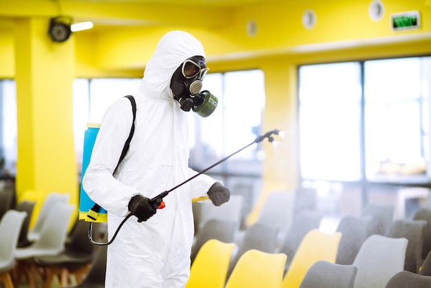 Homem vestindo traje de proteção desinfetando o salão de montagem com produtos químicos em spray para prevenir o coronavírus