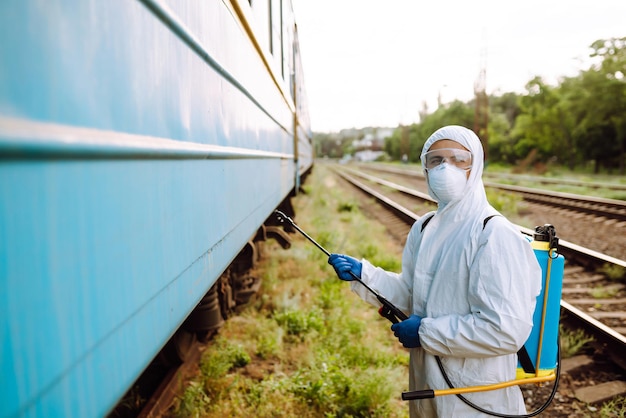 Homem vestindo traje de proteção desinfetando público um trem.