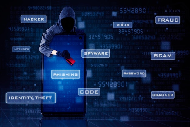 homem vestindo uma balaclava e segurando um cartão de crédito enquanto está de pé atrás de um telefone celular