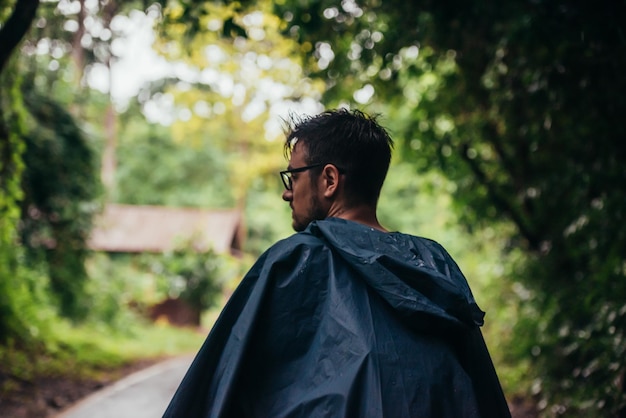 Homem vestindo uma capa de chuva andando no meio de uma estrada ao lado da floresta