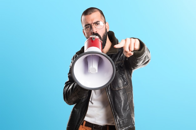 Homem vestindo uma jaqueta de couro gritando por megafone em fundo colorido