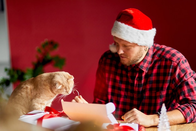 Homem veterinário com chapéu de Papai Noel e gato na mão, fazendo cartões de felicitações de ano novo e Natal