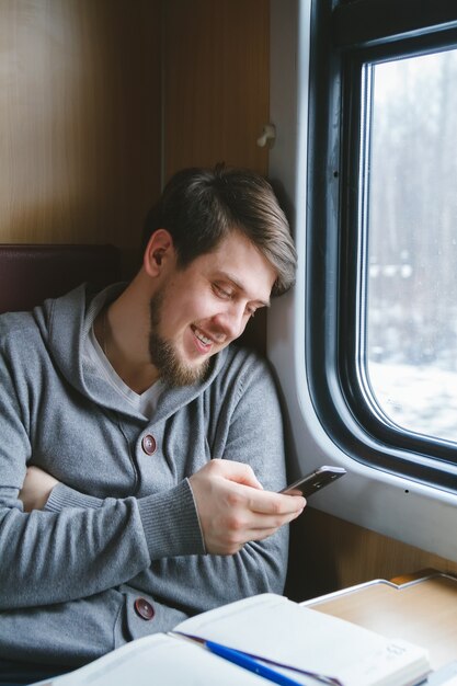 Homem viaja de trem sentado perto da janela usando telefone celular