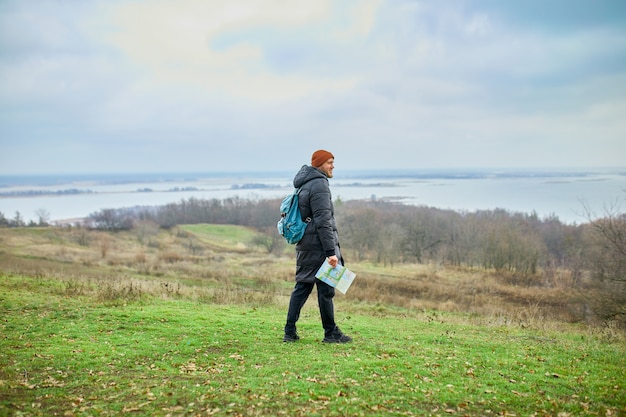 Homem viajante com mochila com mapa na mão em uma parede de rio de montanhas da natureza, conceito de viagens, férias e conceito de caminhadas de estilo de vida