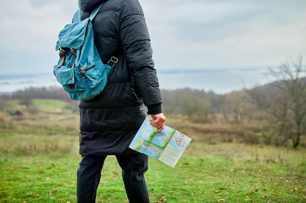 Homem viajante com mochila e mapa na mão em um fundo de montanhas do rio da natureza