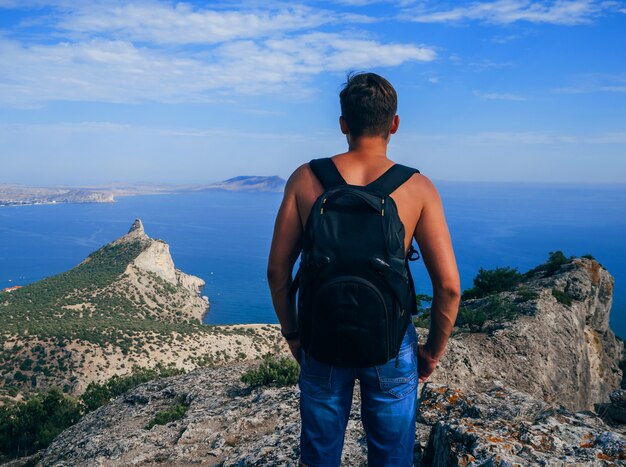 Homem viajante com mochila no topo de uma montanha e olhando para o mar