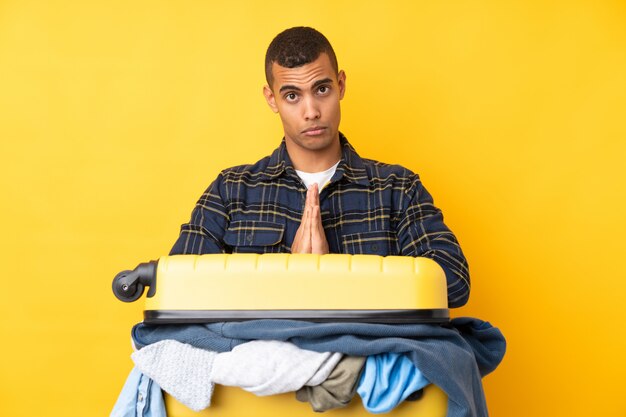 Homem viajante com uma mala cheia de roupas isolado parede amarela suplicando