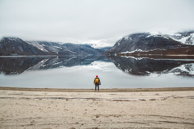 Homem viajante com uma mochila de pé no fundo das montanhas e do lago, apreciando a paisagem