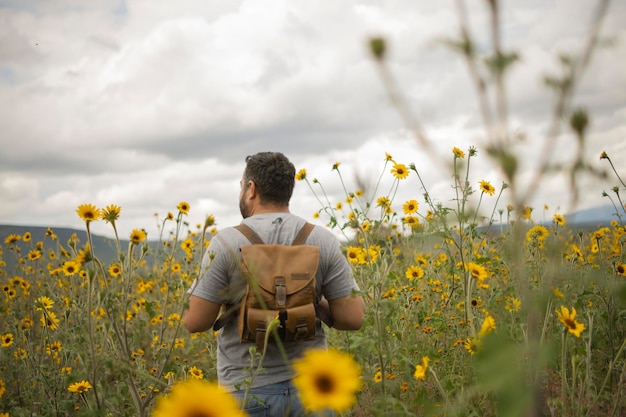 Homem viajante de costas em um campo de flores em um dia nublado