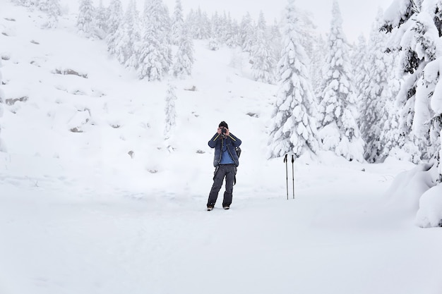 Homem viajante fotografa a natureza em uma área montanhosa e arborizada de inverno