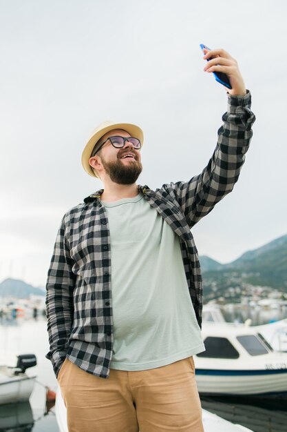 Foto homem viajante tirando selfie de iates de luxo marinhos durante viagens de dia ensolarado e conceito de verão