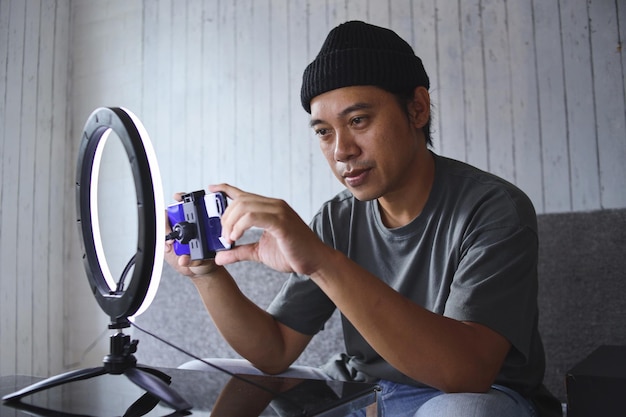 Homem vlogger asiático preparando equipamentos para transmissão ao vivo, configurando o celular antes da gravação.