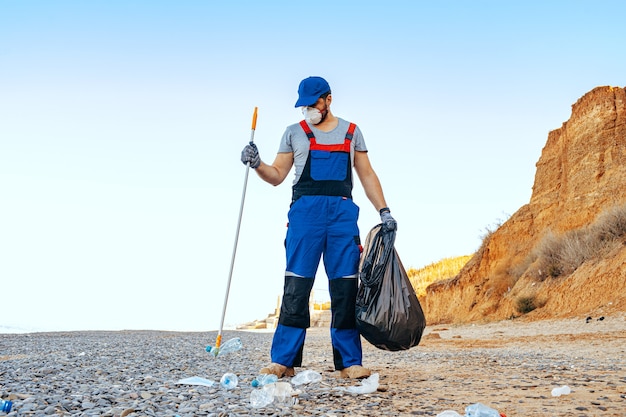 Homem voluntário coletando lixo na praia com um extensor de alcance