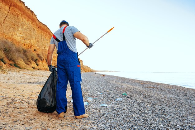Homem voluntário coletando lixo na praia com um extensor de alcance