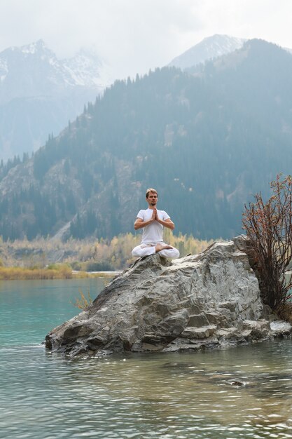 Homem zen jovem em meditação. Ioga ao ar livre no lago de montanha. Exercite Agni Stambhasana.