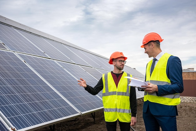 Homens altos com roupas de trabalho estão pensando em instalar painéis solares ao ar livre. O conceito de cuidar de painéis solares sob o céu